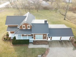 Aerial view of a residential home featuring a sleek metal roof, surrounded by greenery