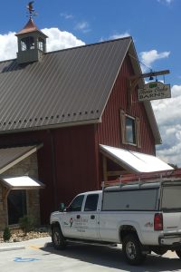 Red barn with standing seam metal roof and roofing truck parked outside.
