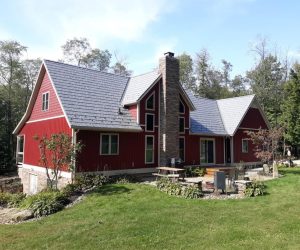 Red house with a gray metal shingle roof and stone chimney.