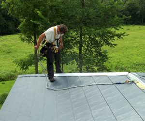 Reputable roofer secured with harness while working on a metal roof.