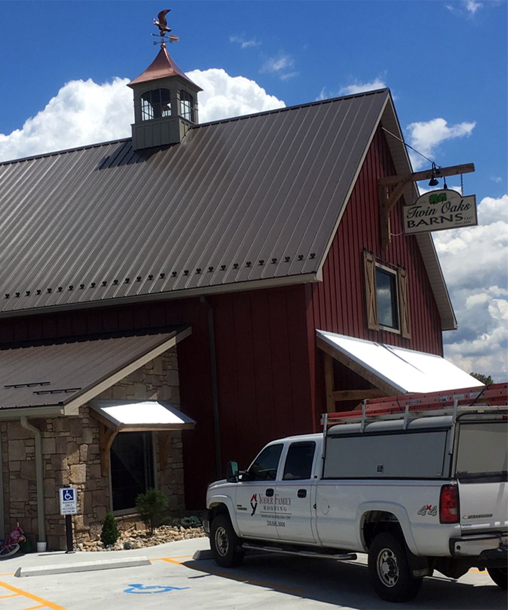 Red barn with standing seam metal roof and roofing truck parked outside.